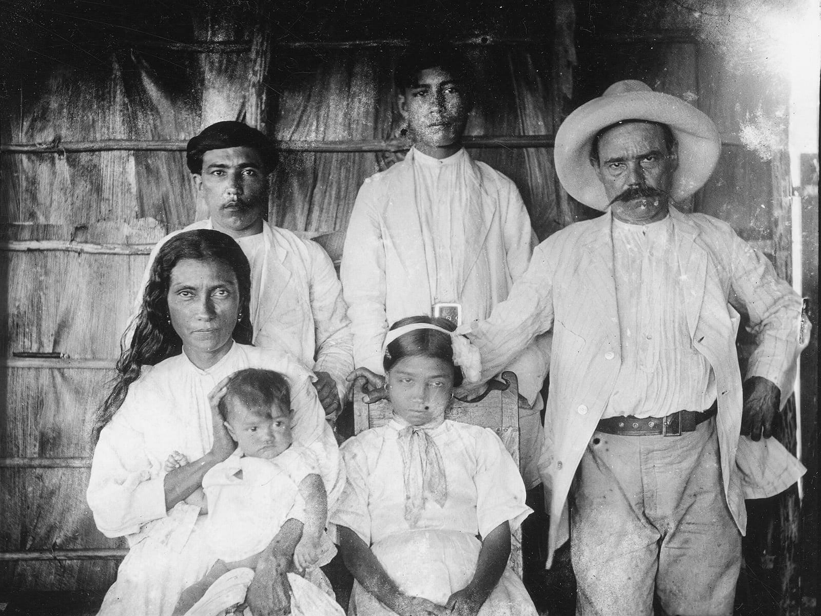 Black-and-white 1919 outdoor family portrait of the Barrientos family in Baracoa, Cuba, with adults and children gathered beside a wooden house.