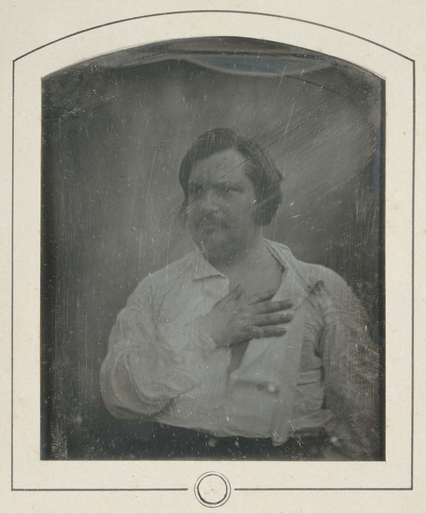 Scratched black-and-white 1842 daguerreotype of Honoré de Balzac in an open-collared white shirt and suspenders, one hand resting on his chest.