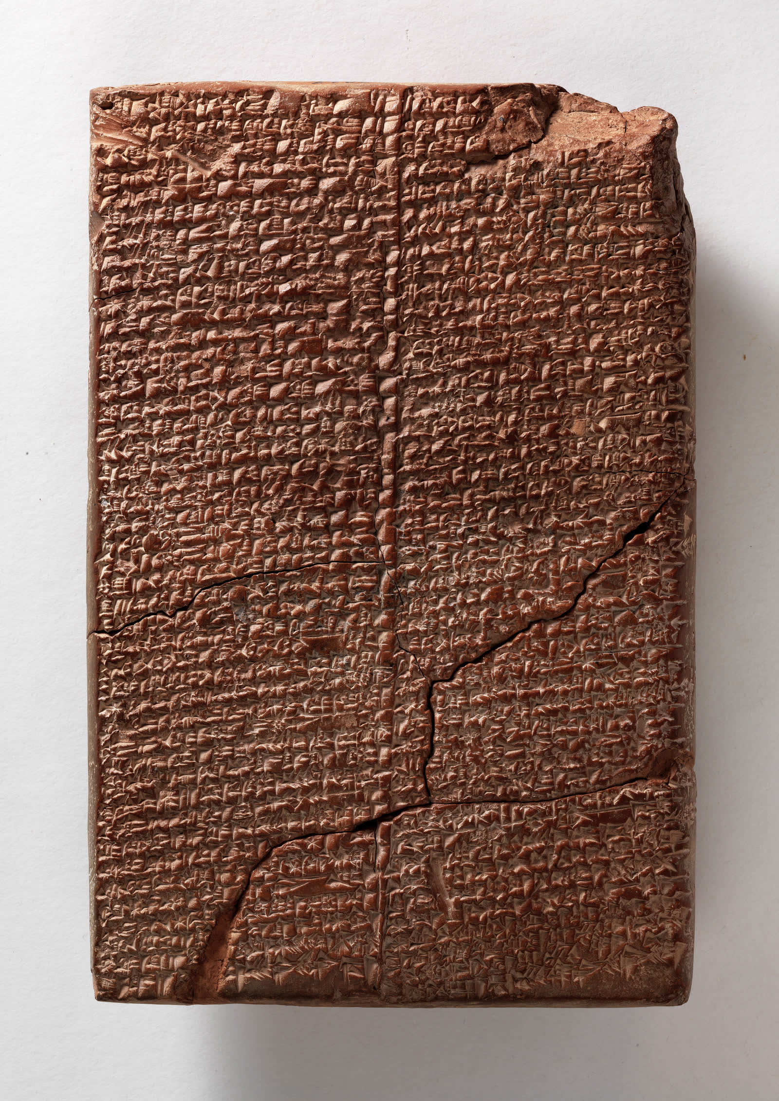 Archival photograph of a tall reddish-brown clay tablet densely inscribed with cuneiform in three columns and visibly repaired across several ancient breaks.