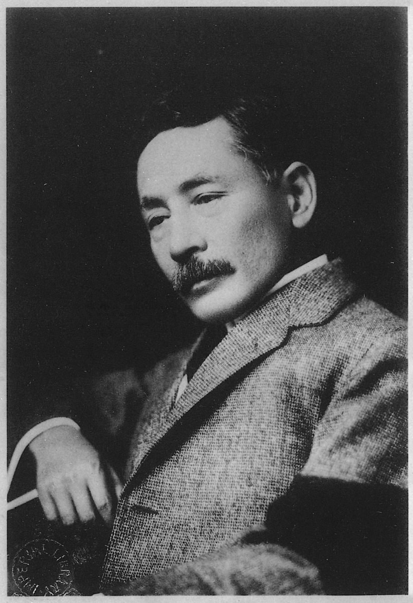 Black-and-white archival portrait of Natsume Soseki seated in three-quarter view, wearing a textured jacket and resting one arm on a chair.