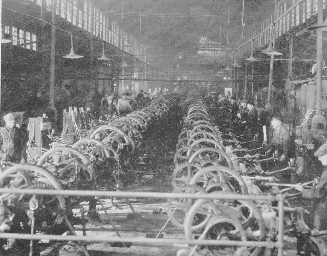Black-and-white archival photograph of workers standing along two banks of belt-driven nail-cutting machines inside LaBelle Cut Nail Works in Wheeling.