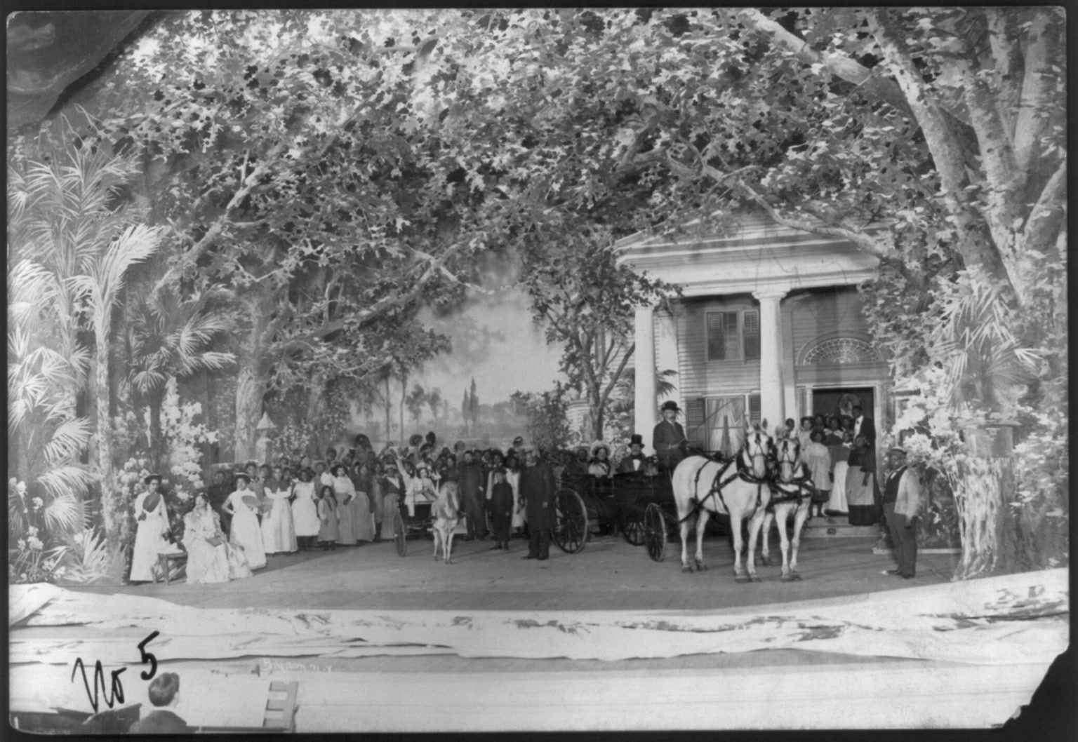 Black-and-white 1901 stage photograph showing dozens of Uncle Tom's Cabin performers on a plantation-house set, with oversized trees, a small cart, and a horse-drawn carriage.