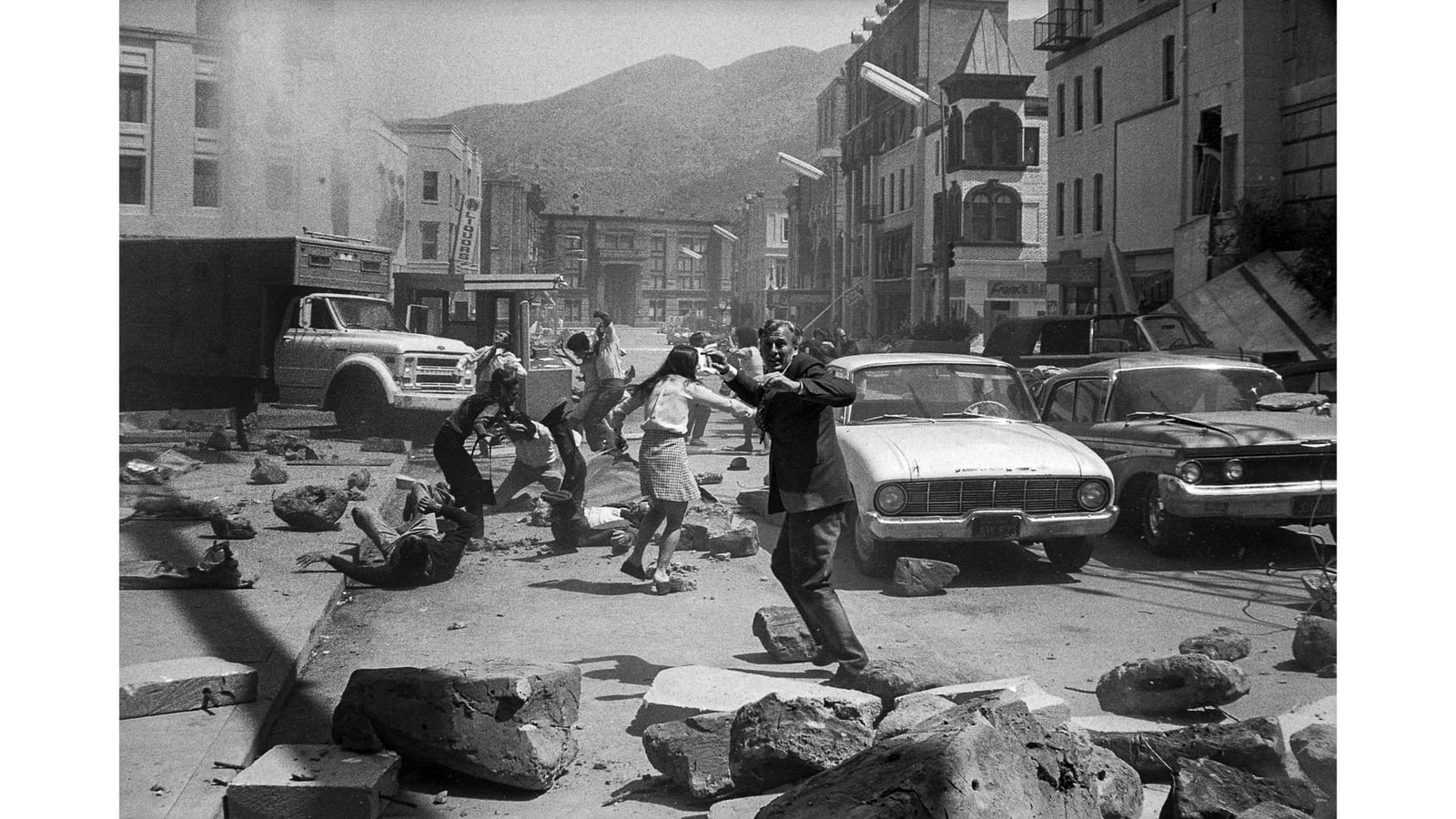 1974 年电影《大地震》的一张幕后档案照片中，演员们在遍地瓦砾的洛杉矶街景里躲避轻质仿造巨石。
