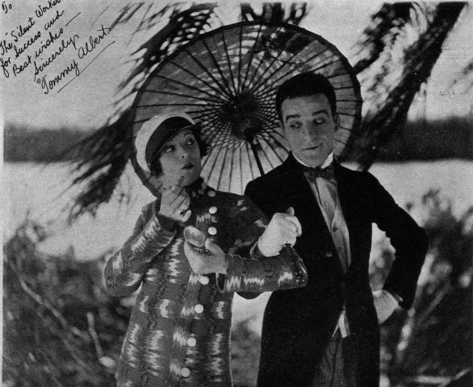 1927 年无声喜剧《Great Guns》的黑白档案剧照，演员卡门·德·阿科斯与埃默森·罗梅罗在一把阳伞下表演。