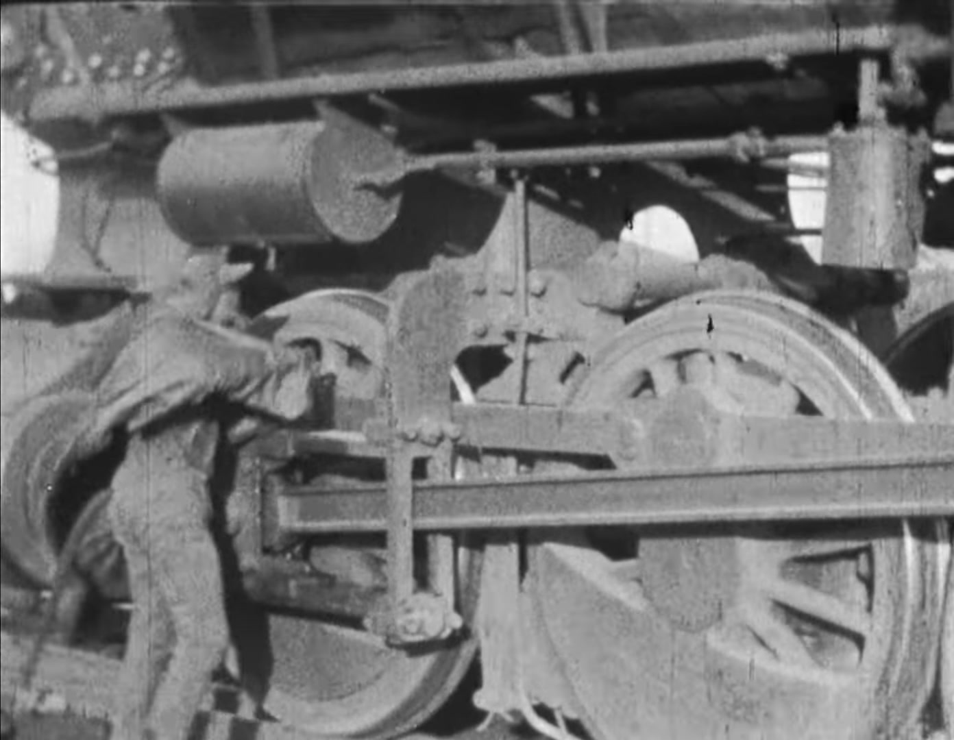 Black-and-white restored frame from Hell-Bound Train showing the film's horned devil crouched beside the wheels and connecting rods of a locomotive.