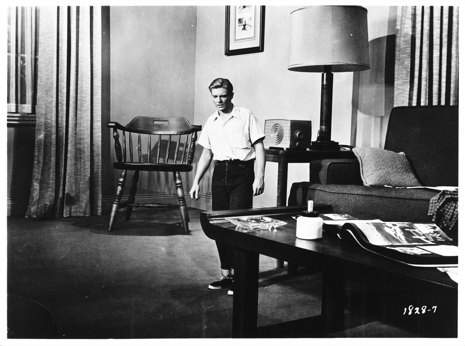 Black-and-white Universal promotional photograph for The Incredible Shrinking Man showing Grant Williams as Scott Carey at reduced scale among living-room furniture.