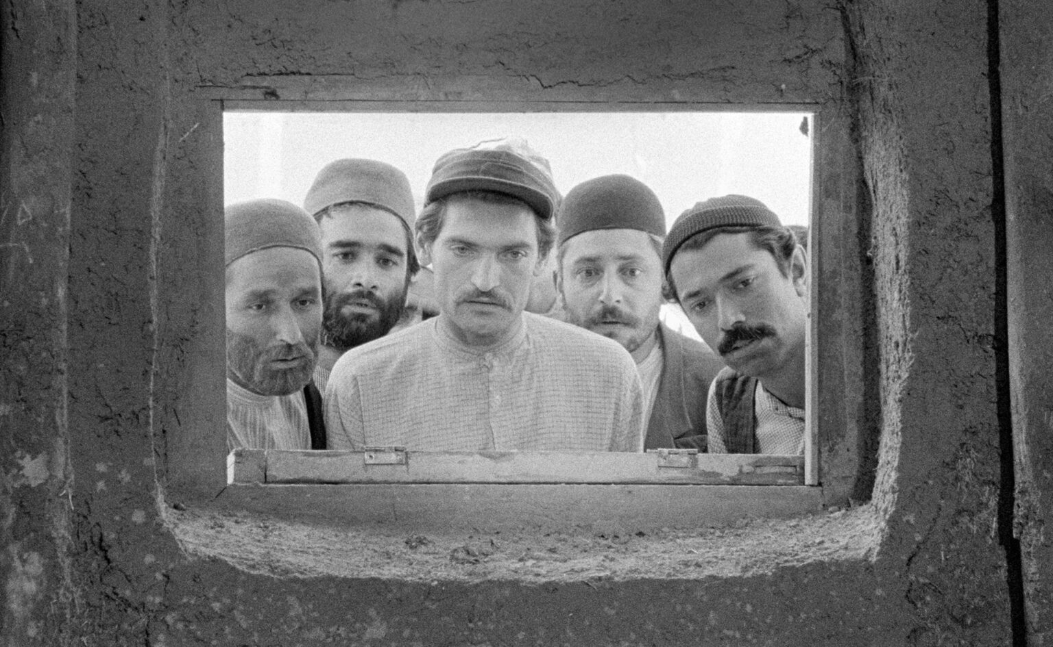 Five village men peer through a small rectangular window in a black-and-white archival still from The Cow.