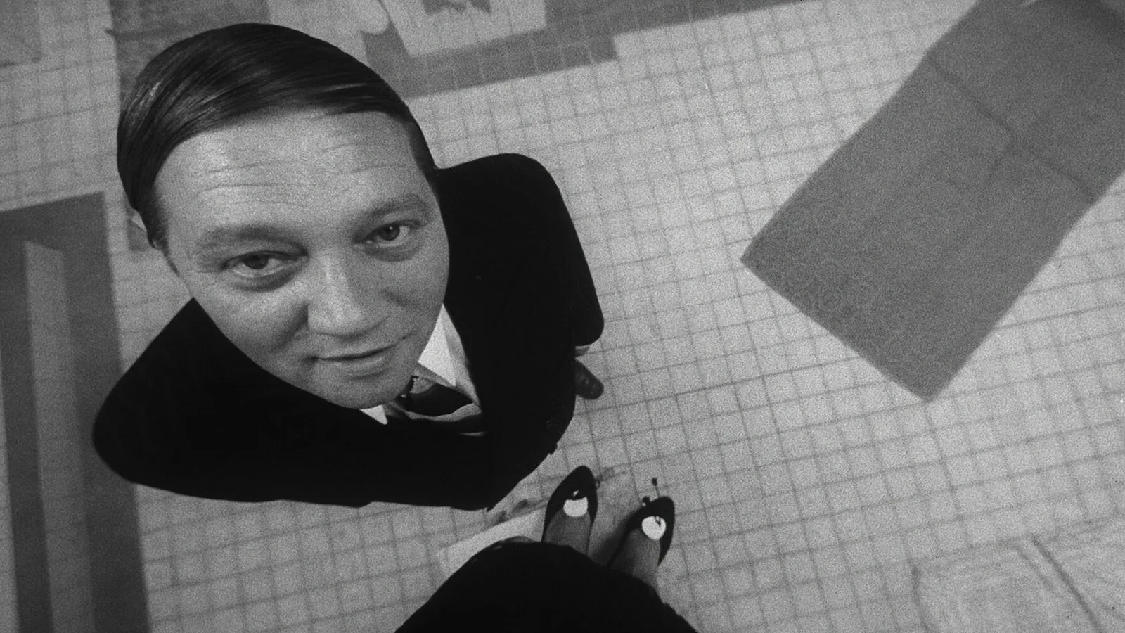 Karel Kopfrkingl looks up at the camera from a steep, distorting high angle on a tiled floor.