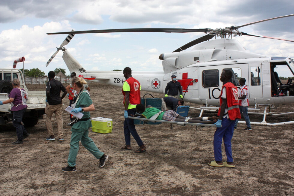 International Committee of the Red Cross and South Sudan Red Cross medical staff carrying a wounded patient on a stretcher beside an ICRC helicopter in Akobo, South Sudan.