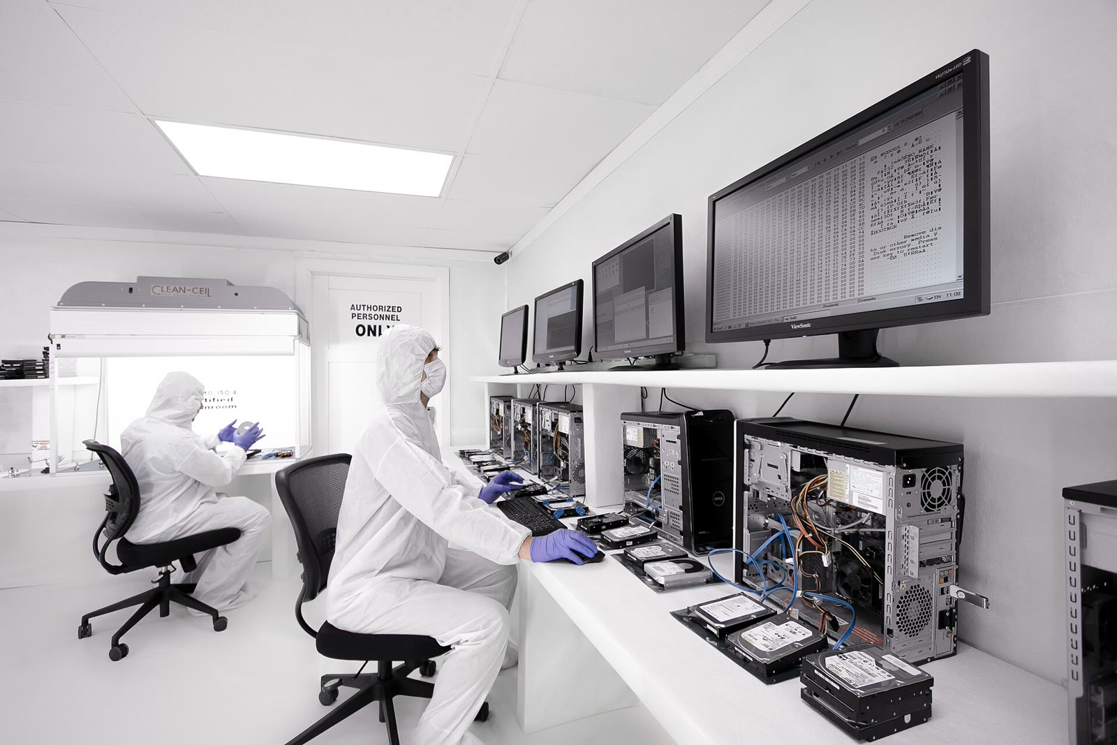 Two digital-forensics examiners working among open computers and hard drives in a bright laboratory.