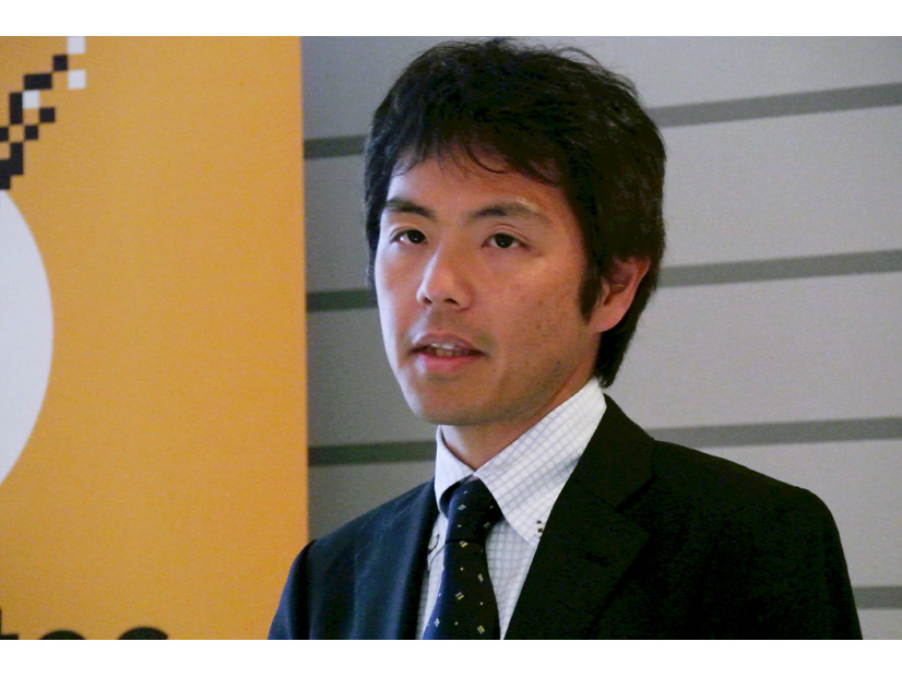 Tetsuya Adachi 在东京举行的赛门铁克新闻简报会上发言，身后露出一部分黄色演示背景。
