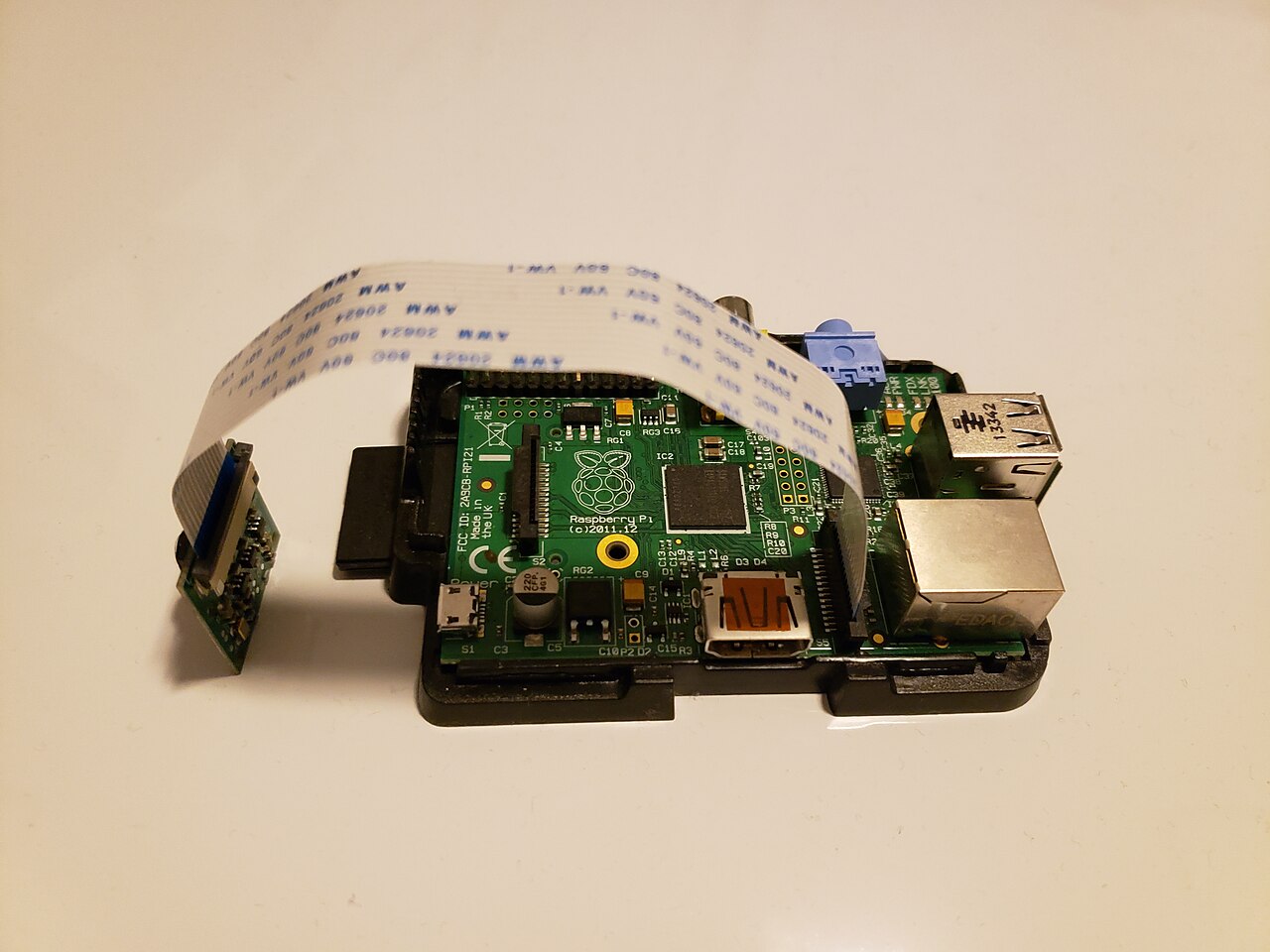 A Raspberry Pi 2 board connected by a looping white ribbon cable to a small camera module resting beside it.