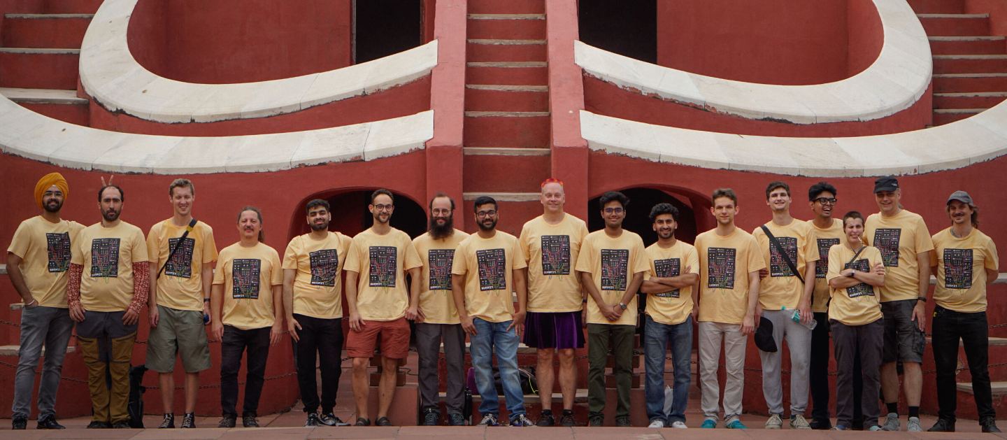 Seventeen MetaBrainz contributors pose between red sandstone walls at New Delhi's Jantar Mantar observatory during their 2024 summit.