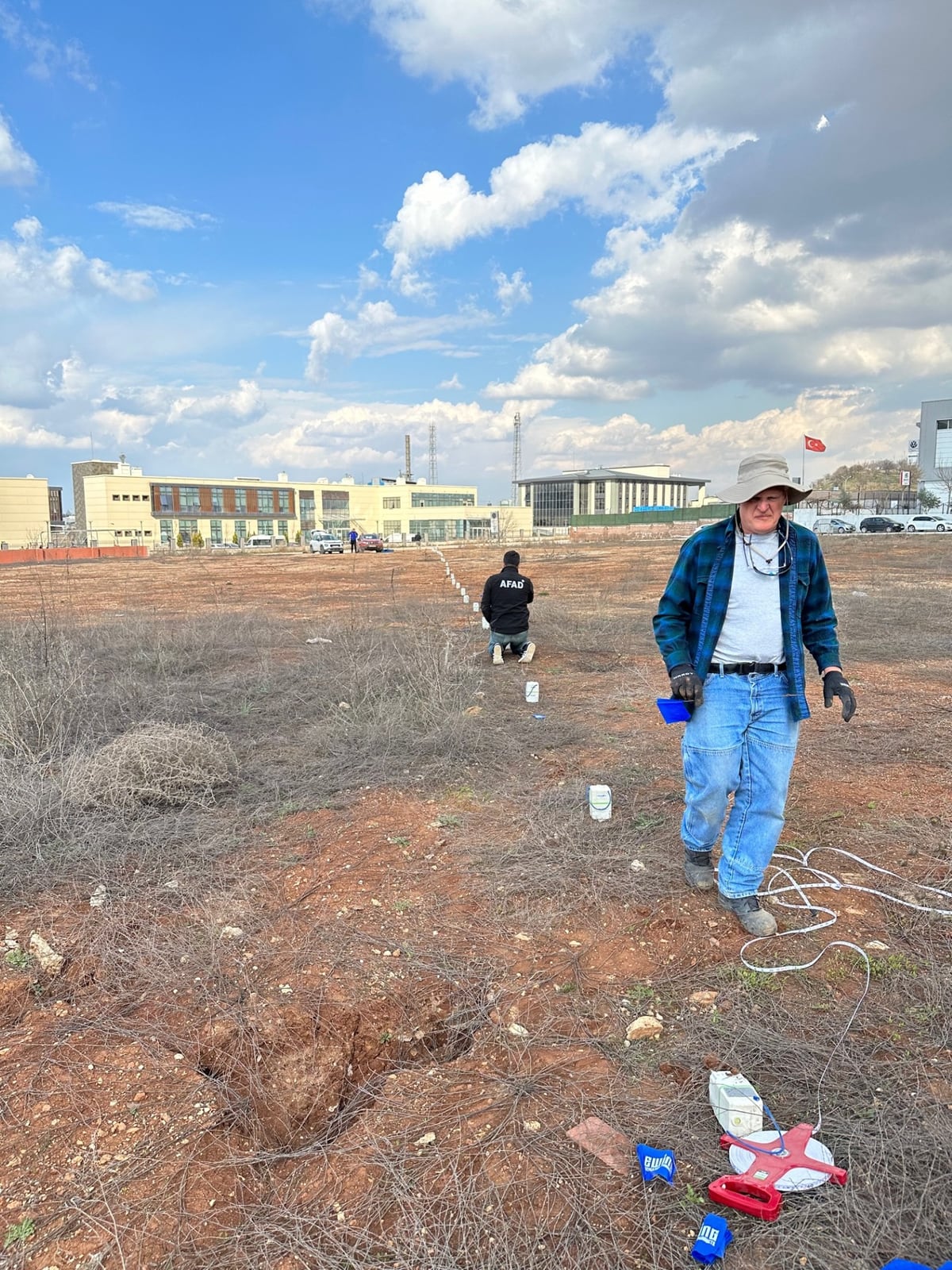 Two field scientists installing a long line of nodal seismometers across an open site in Gaziantep, Turkiye.