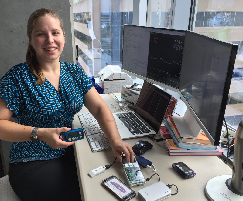 OpenAPS 联合创始人 Dana Lewis 站在一套早期设备旁，整套设备由 Raspberry Pi、无线电硬件、血糖监测设备和胰岛素泵组装而成。