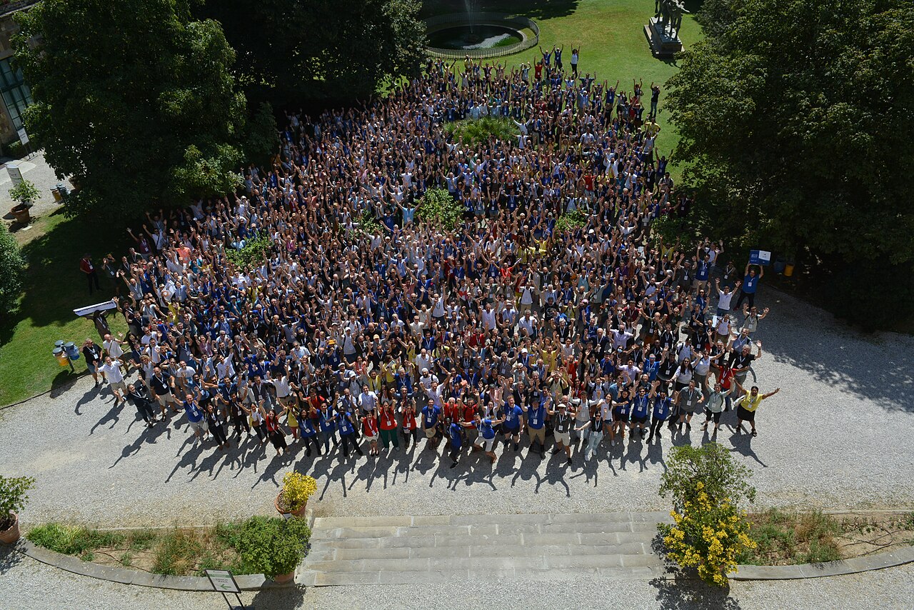 Hundreds of FOSS4G 2022 participants gathered for a group photograph in a courtyard in Florence.