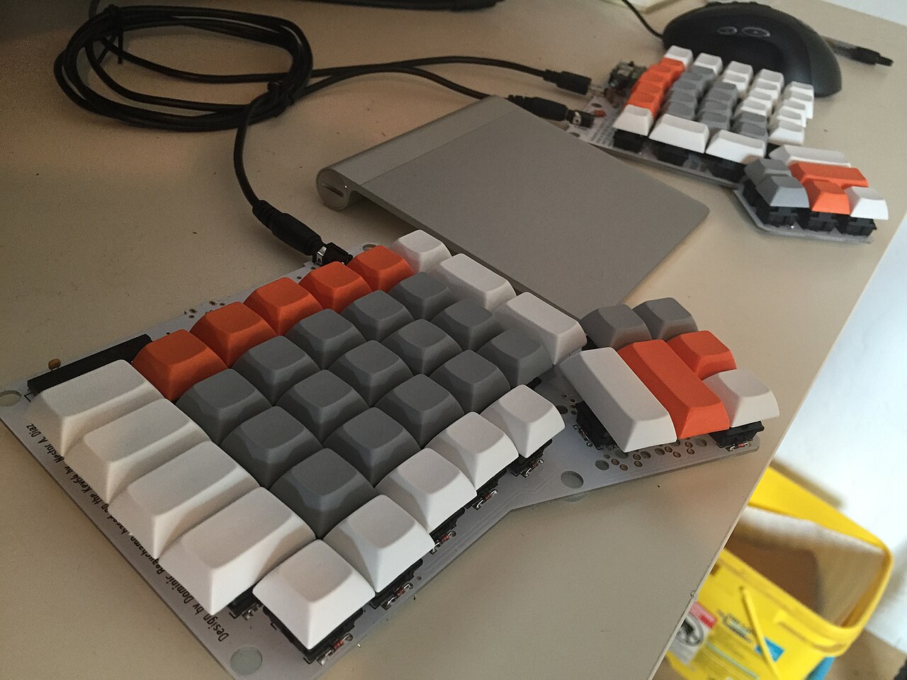 Two uncased halves of an ErgoDox keyboard sit around a trackpad, with key switches, circuit boards, controllers, and connecting cables exposed.