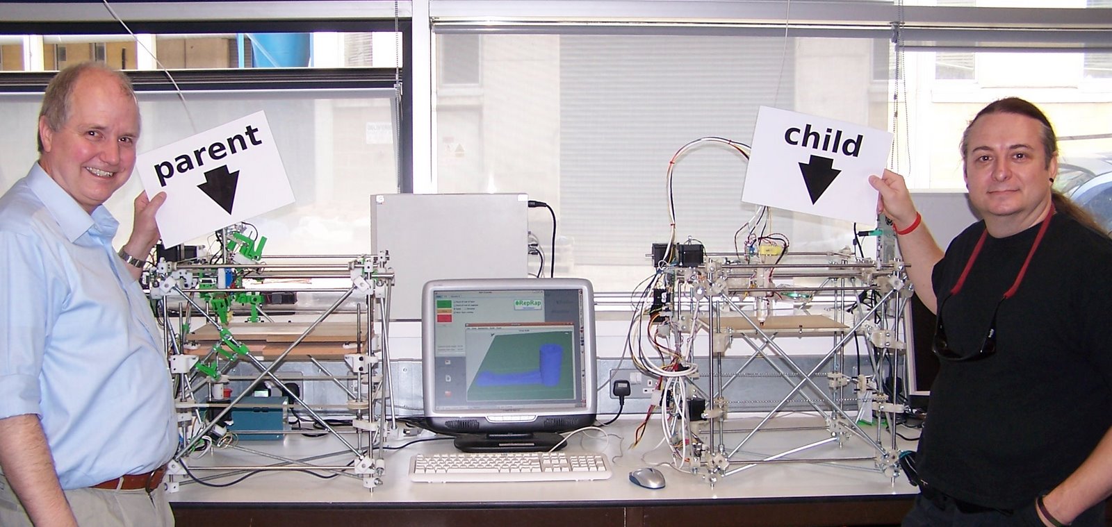 Adrian Bowyer 与 Vik Olliver 站在巴斯大学的 RepRap 母机和首台可完整运行的子机旁。