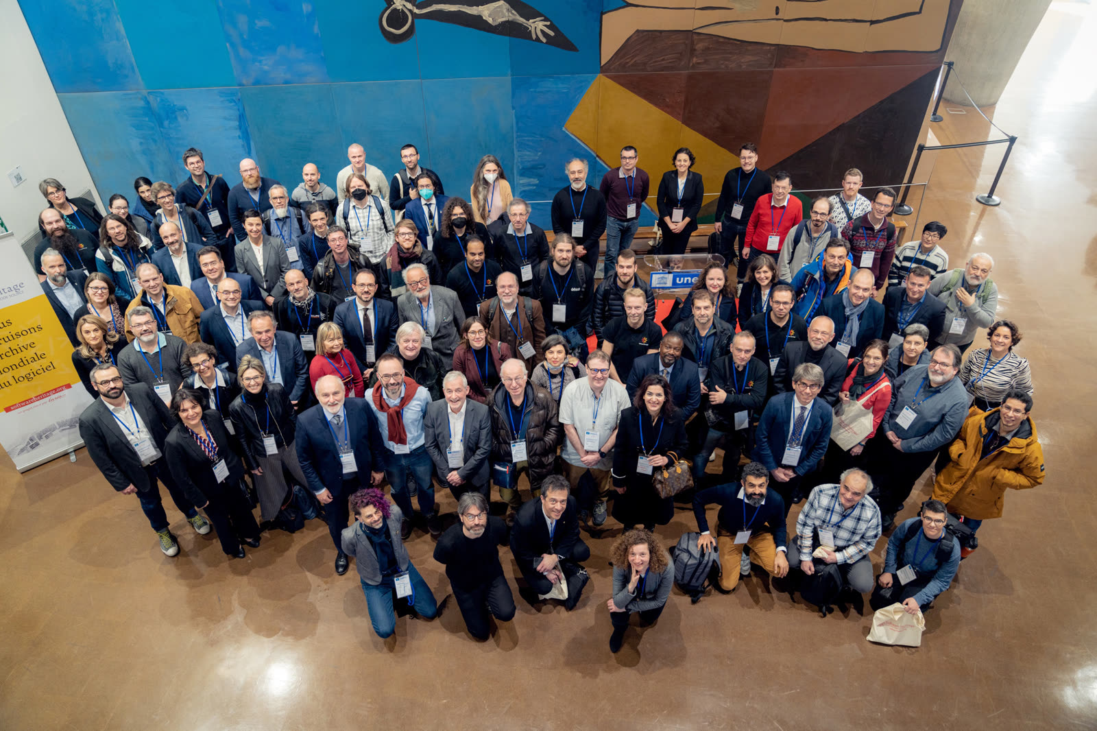 Software Heritage community members gathered in a UNESCO conference hall beneath a mural and beside a source-code heritage banner.