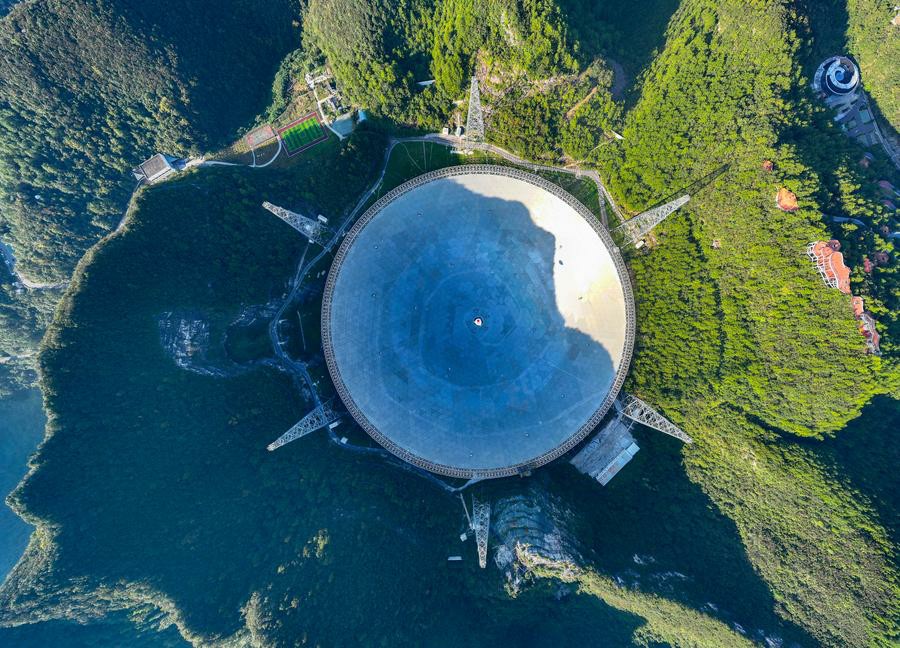 The FAST radio telescope's broad dish set among green hills in Guizhou.