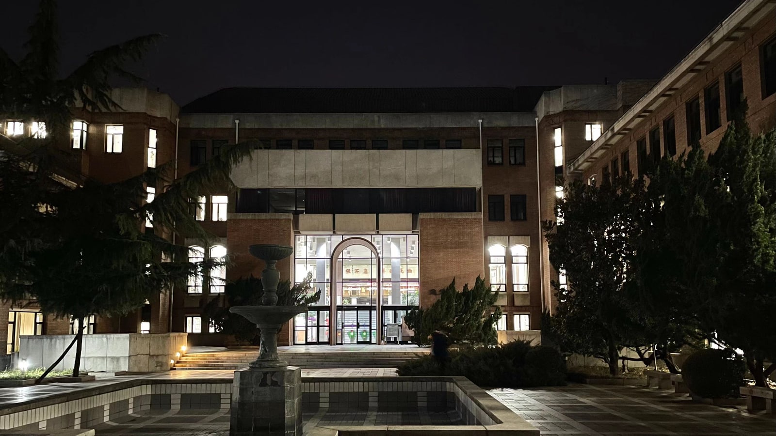 Tsinghua University's illuminated West Library behind a courtyard fountain and trees at night.