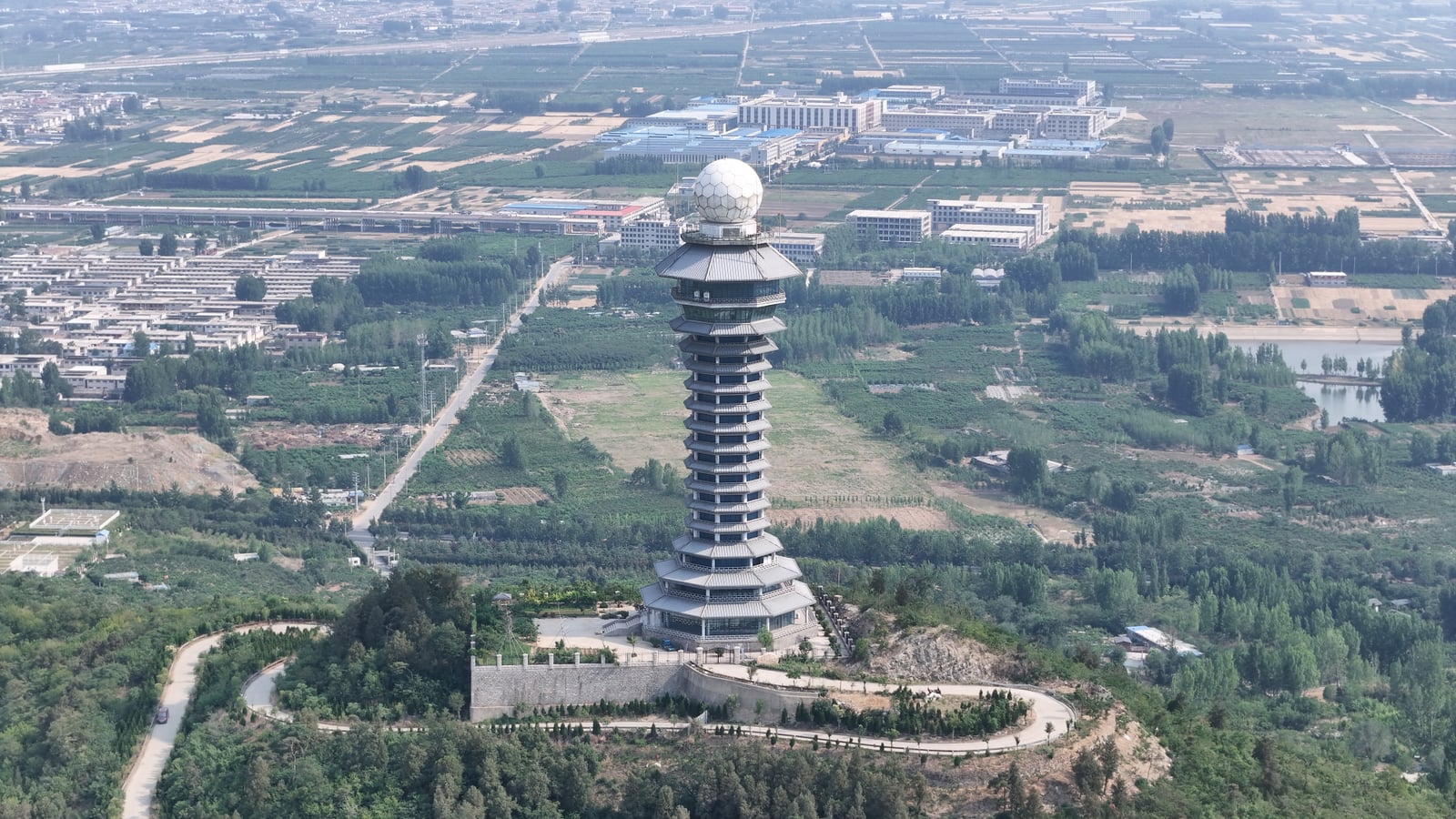 A pagoda-shaped weather-radar tower with a white spherical radome rises above trees, fields, and buildings in Linyi, China.