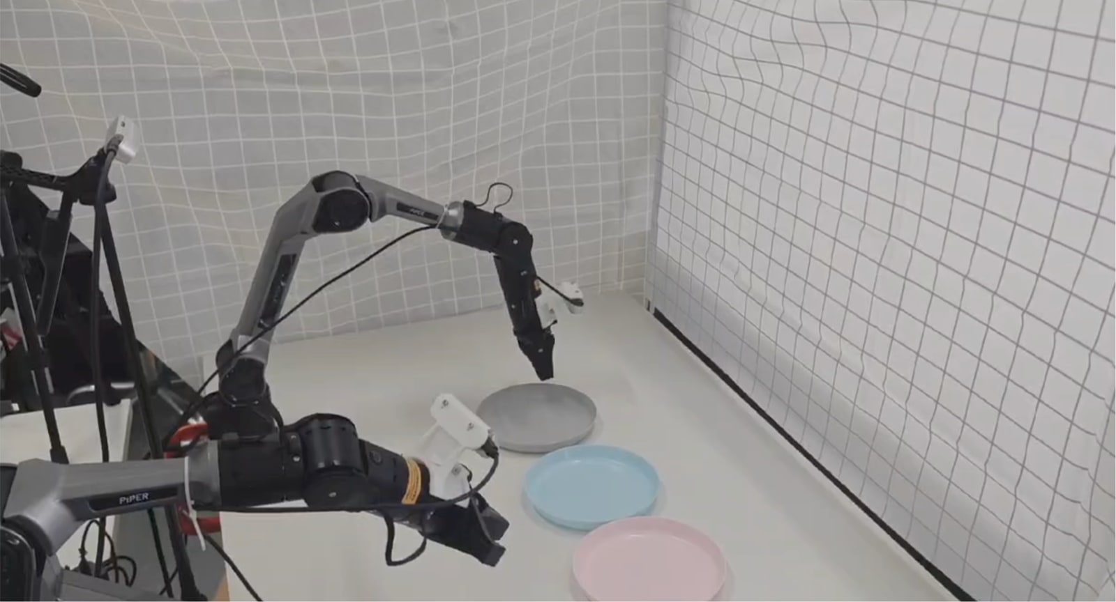 Two physical robot arms working with plates on a tabletop during a RoboTwin manipulation task.