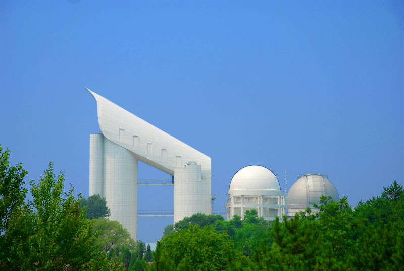 The long, inclined LAMOST telescope building at Xinglong Station, surrounded by green hills.