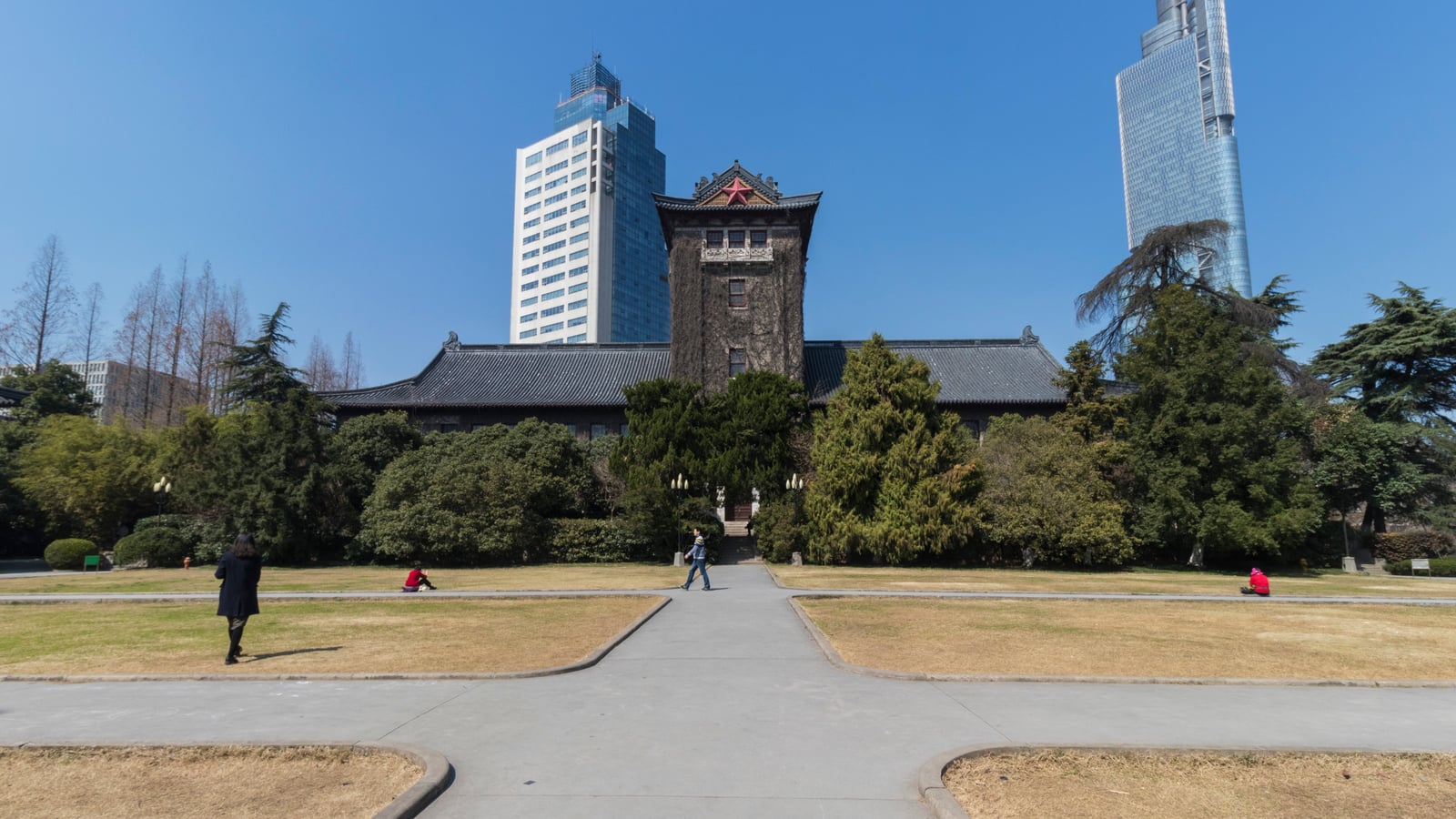 Nanjing University’s ivy-covered North Building faces a lawn and paths, with modern towers rising behind its tiled roof.