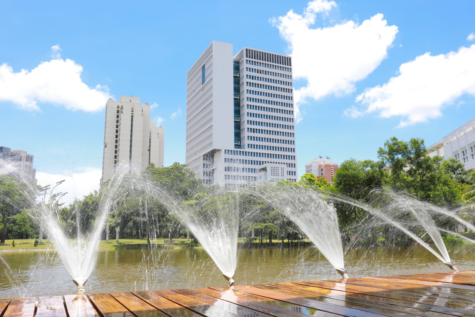 The Information Building at Tsinghua Shenzhen International Graduate School behind fountains, a pond, and trees.