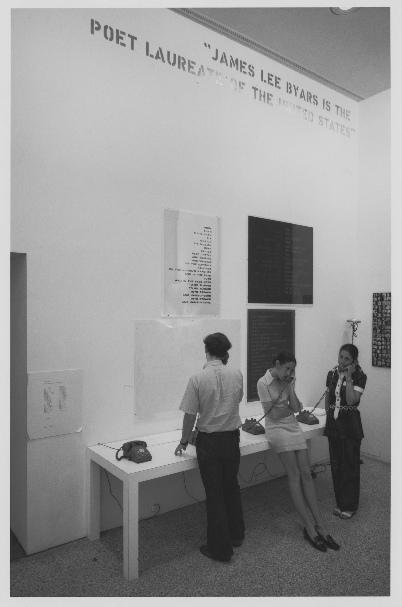 黑白照片中，3名观众在纽约现代艺术博物馆1970年的 Information 展览上，通过转盘电话聆听约翰·吉奥诺的 Dial-A-Poem。