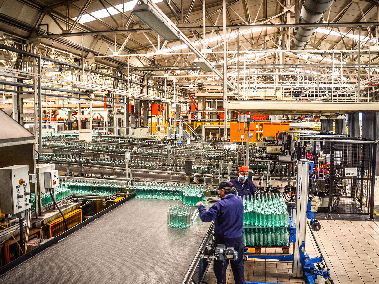 Two workers handle rows of green glass bottles beside conveyors inside O-I's Villotta plant in Italy.