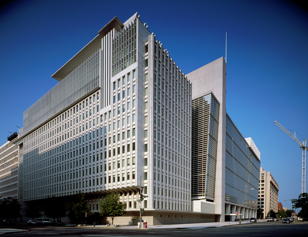 Tall white window fins on the IMF headquarters rise above a Washington street corner beneath a clear blue sky.