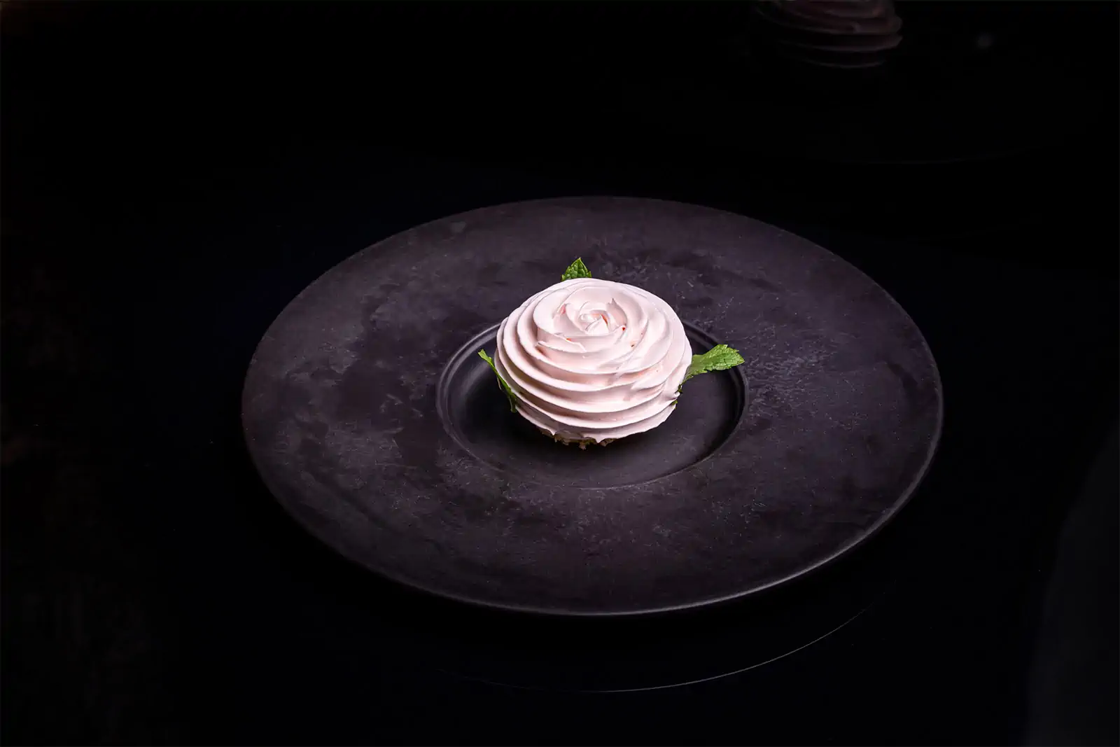 Pale pink meringue piped into a rose, with mint leaves, on a broad dark plate at Cosmos in Sofia.