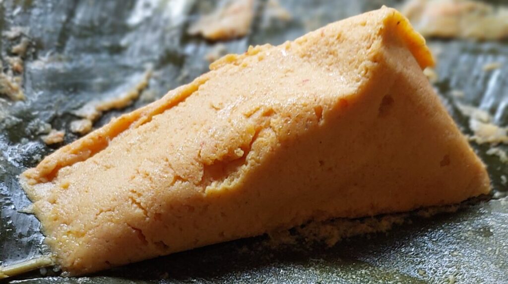 A wedge of golden moin moin resting on an opened dark green cooking leaf, with its fine, moist texture visible.