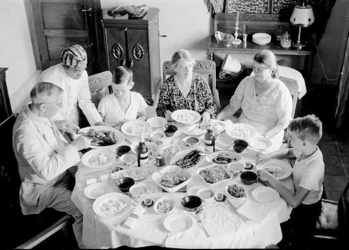 The Japing family and relatives seated around a table crowded with small dishes, with a server standing on the left.