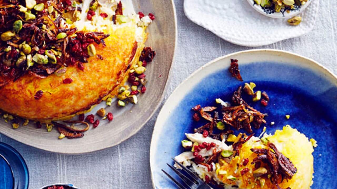 A golden tahchin with a wedge removed, beside a plated slice topped with fried onions, barberries and pistachios.