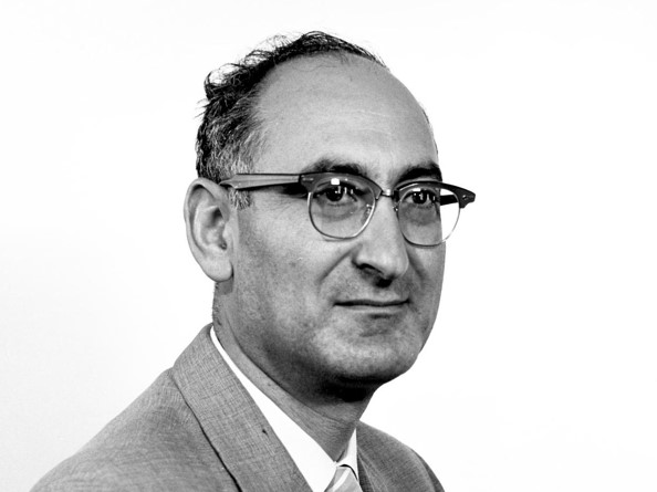Avedis Donabedian wearing dark-rimmed glasses and a suit in a black-and-white archival portrait.