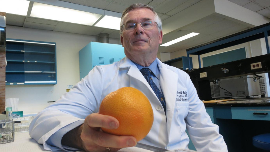 Clinical pharmacologist David Bailey in a laboratory, wearing a white coat and holding a grapefruit.