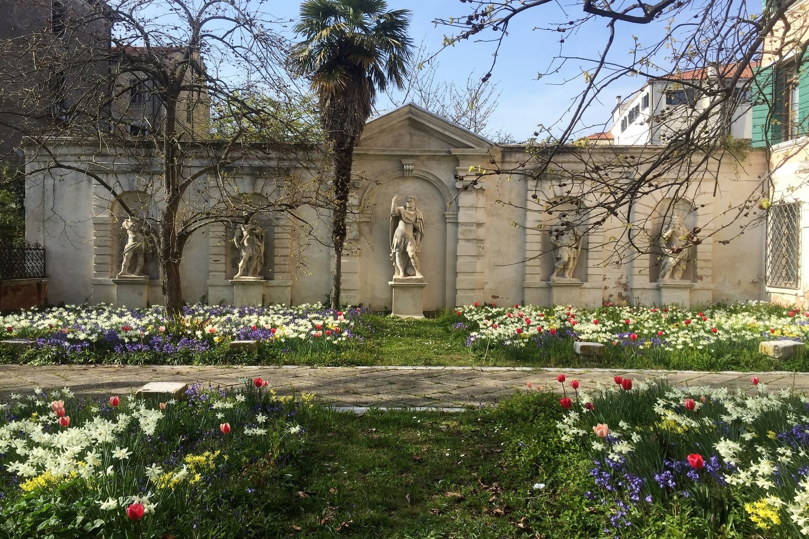 Spring flowers and budding trees in front of a garden wall lined with statues at Palazzo Soranzo-Cappello in Venice.