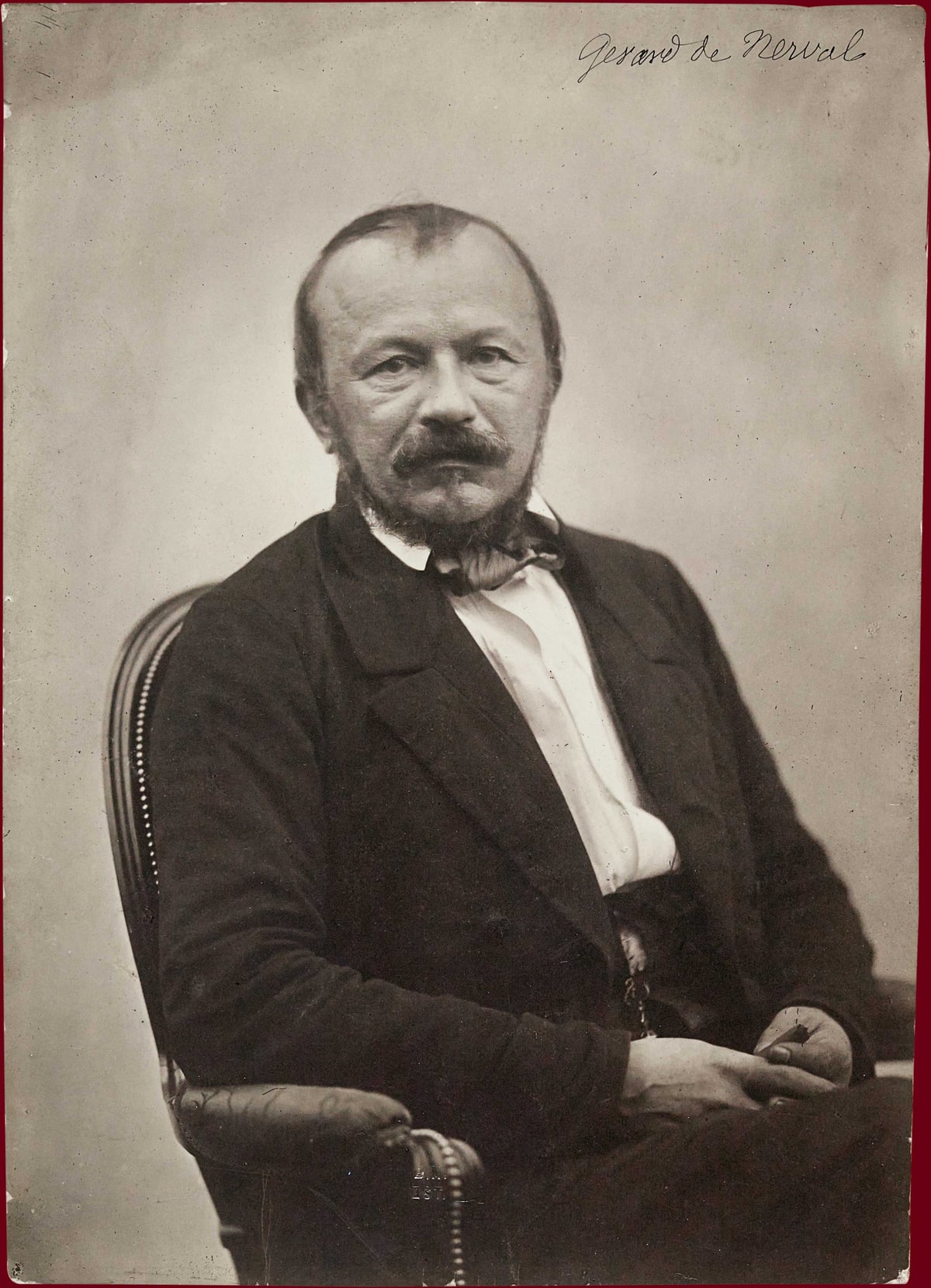 Sepia photographic portrait of Gérard de Nerval, seated in a dark coat with his hands resting together in his lap.