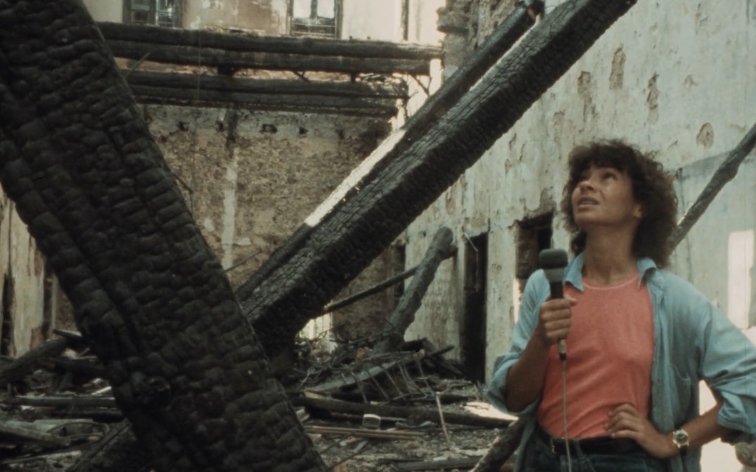 Jocelyne Saab holds a microphone while standing among broken walls and rubble inside her destroyed family home.