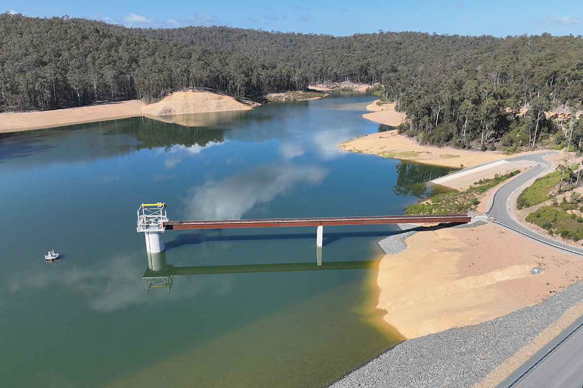 Water surrounds an outlet tower and its access bridge at Eurobodalla's Southern Storage Facility, with exposed banks and forest beyond.