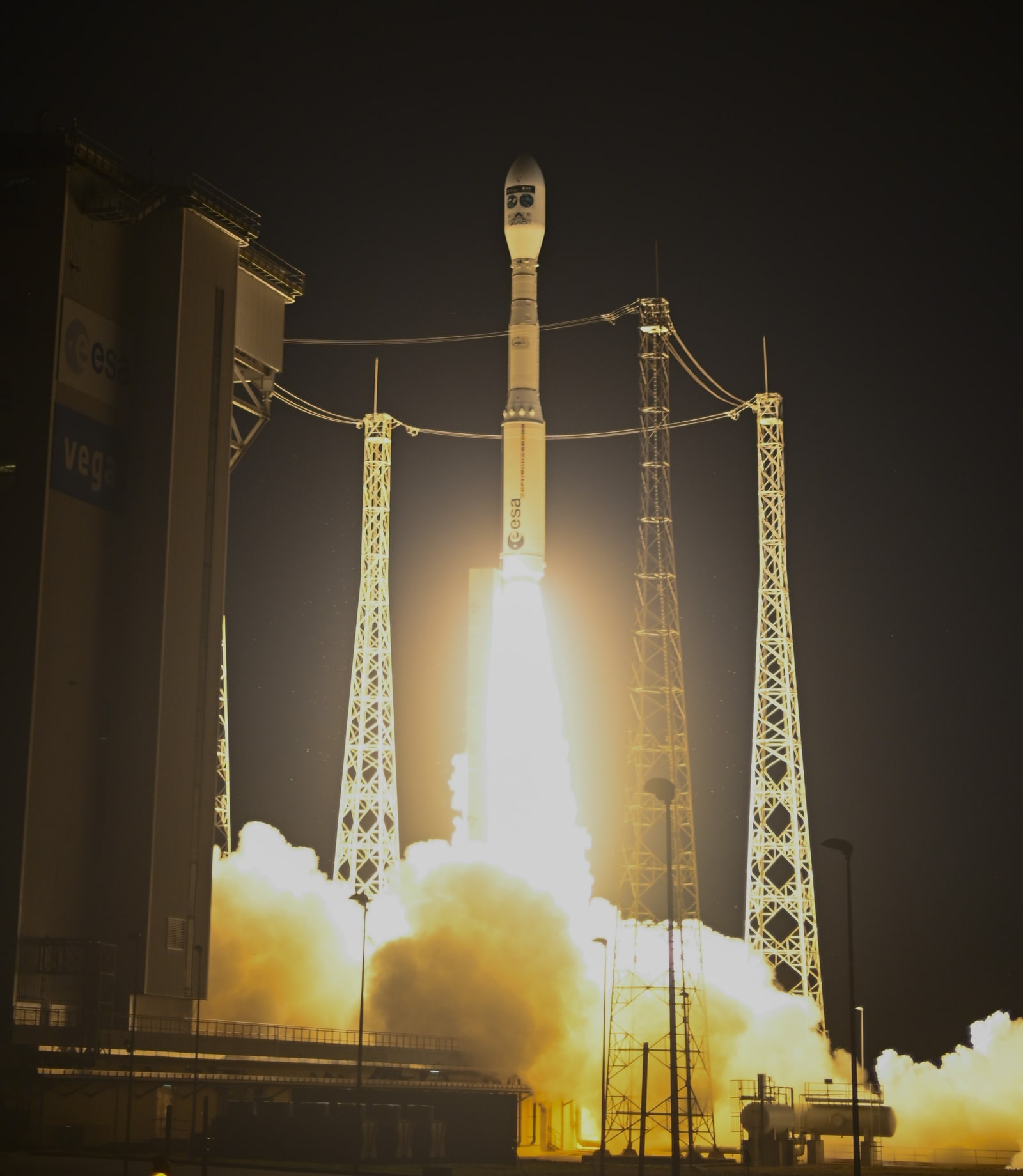A Vega-C rocket rises above its launch pad at night, trailing a bright exhaust plume through illuminated clouds of smoke.