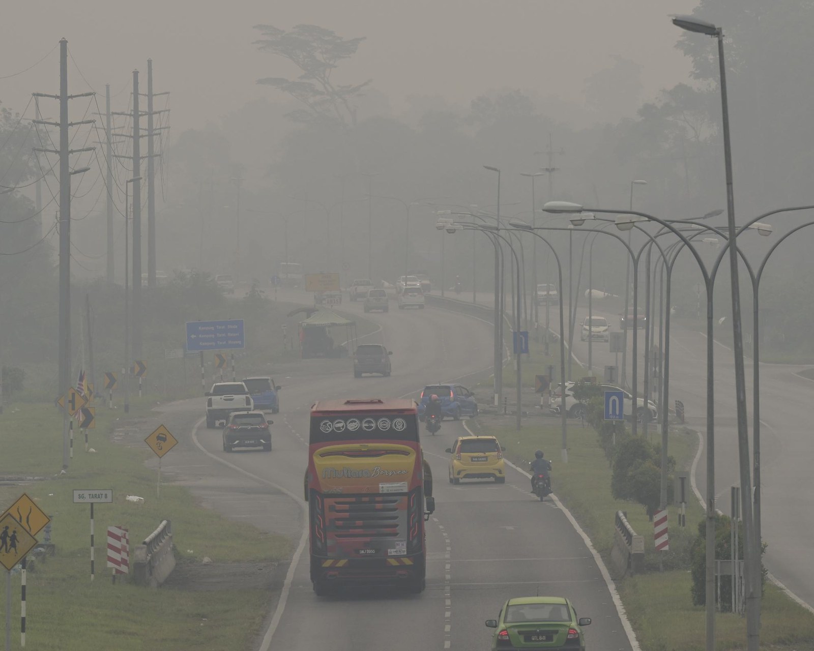 Vehicles travel along a divided road in Serian as dense grey haze obscures trees and the distance.