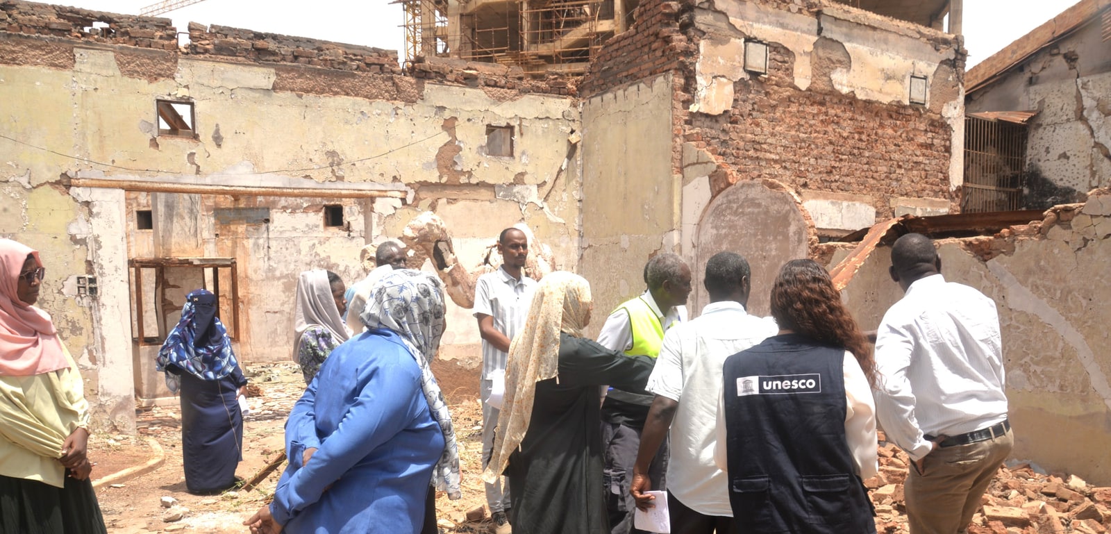UNESCO and Sudanese heritage professionals inspect a roofless building with damaged brick walls.