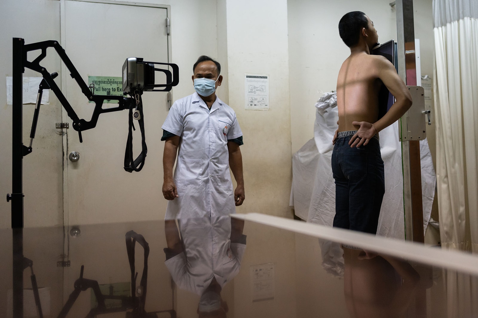 A radiologic technologist stands beside portable X-ray equipment as a patient faces a detector in Phnom Penh, Cambodia.