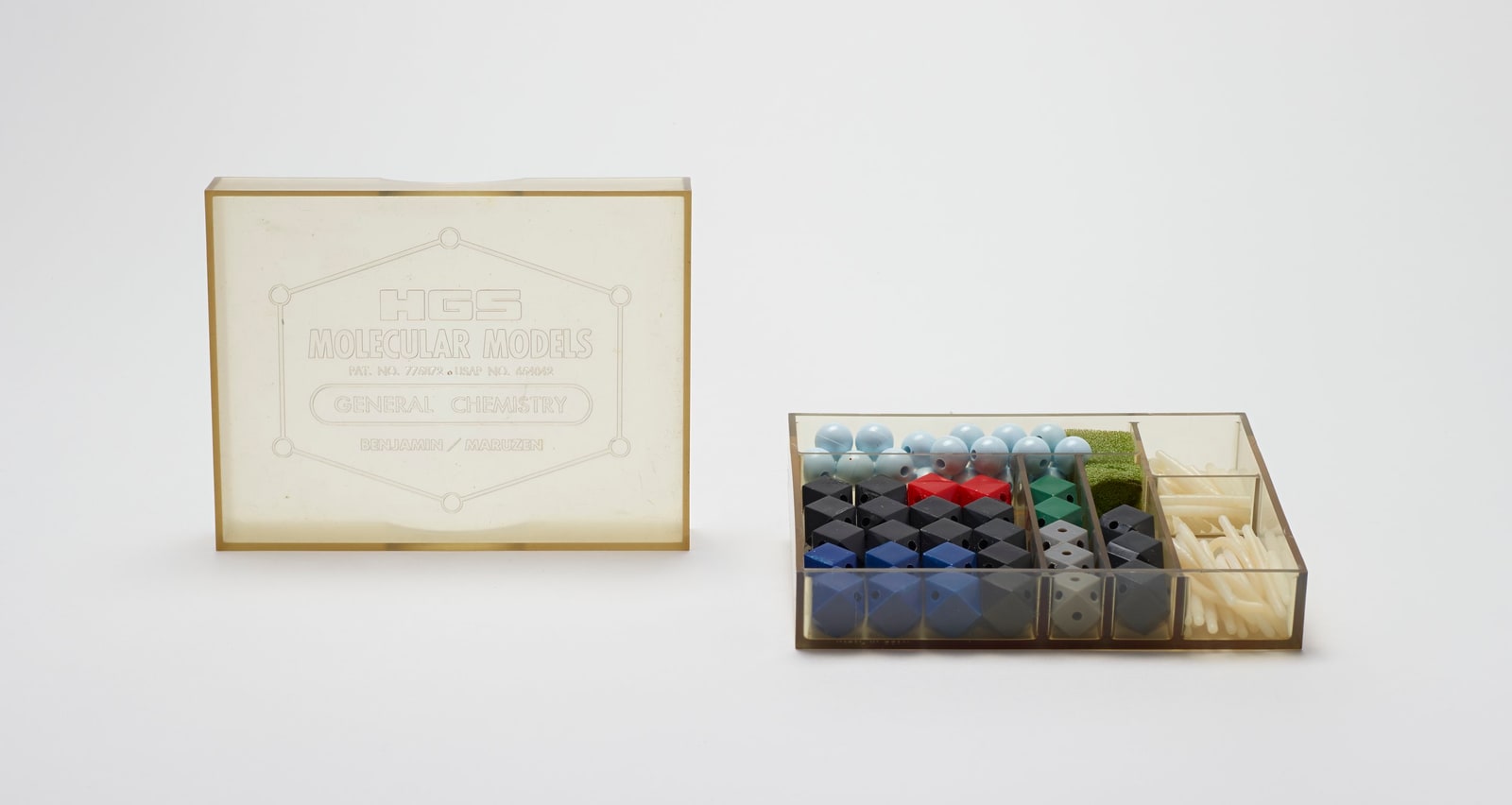 An open HGS chemistry model kit with colored blocks, pale blue spheres, and white connecting rods beside its labeled translucent lid.