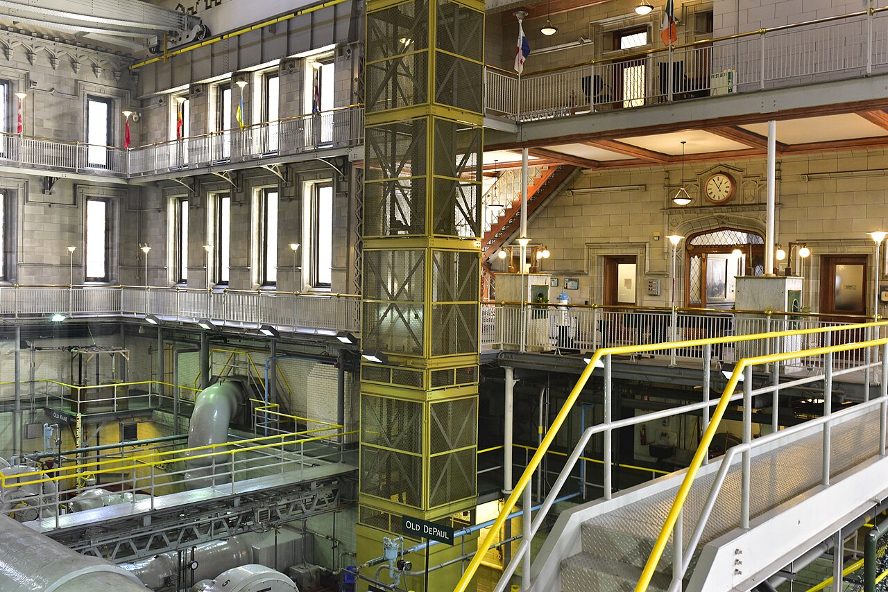 Large pipes and pumping machinery beneath yellow-railed walkways inside Chicago Avenue Pumping Station.