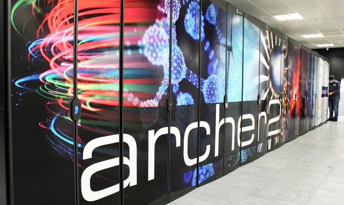 A row of ARCHER2 supercomputer cabinets with colorful printed panels, large white lettering, and a person at the far end.